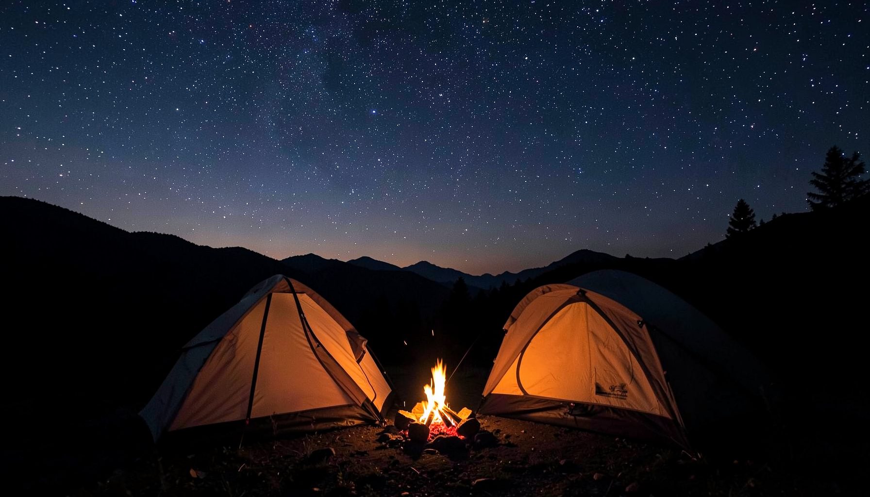 A campfire glowing at twilight beside a pitched tent, with a star-filled sky emerging over a silhouetted mountain range