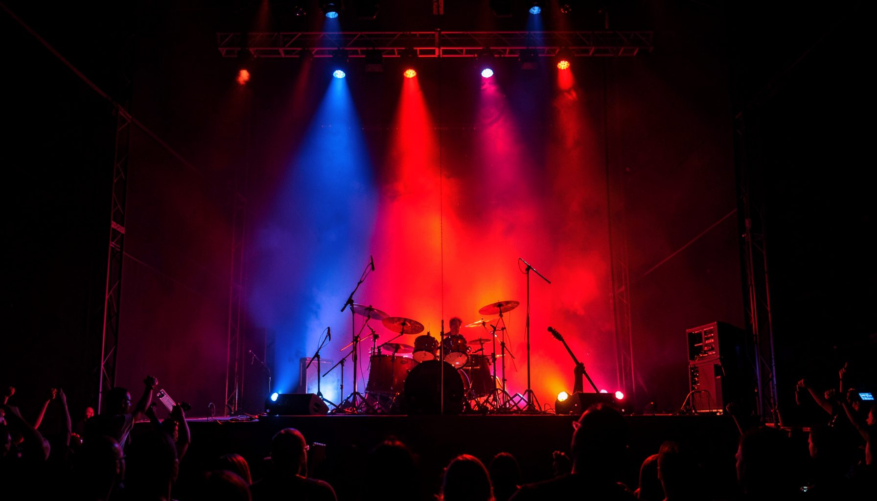 Concert stage bathed in red and blue light with silhouetted instruments, energetic rock show atmosphere