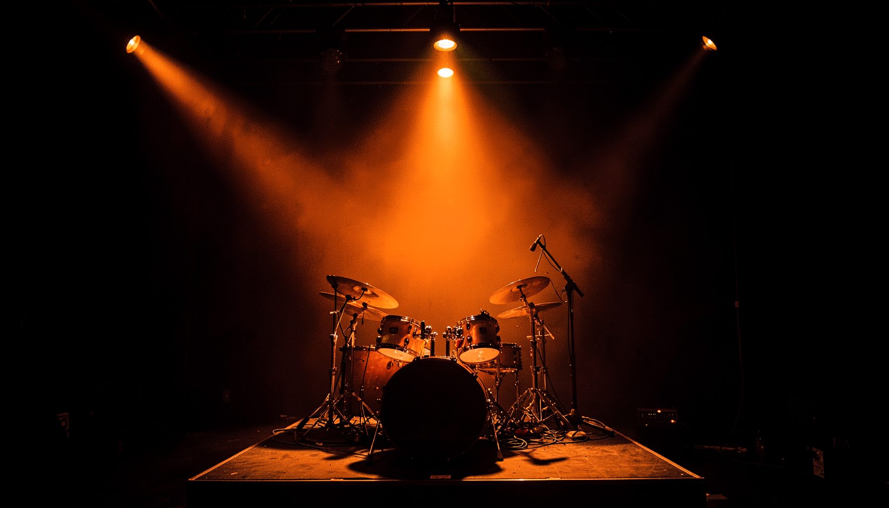 Drum kit under dramatic overhead lighting, deep shadows and warm amber glow, live session feel