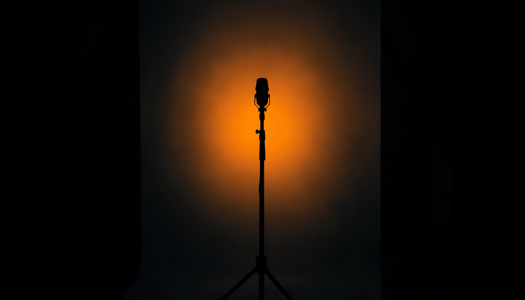 Dark, moody studio scene with warm amber and deep navy tones, a microphone stand silhouetted against soft backlight.