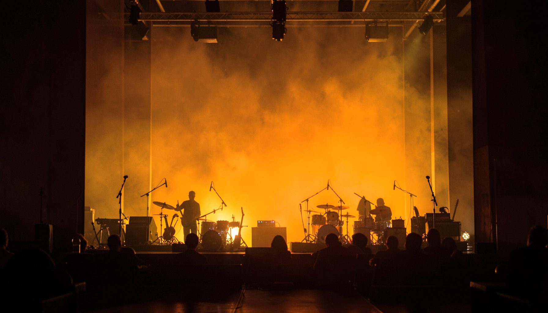Warm amber and gold stage wash with silhouetted instruments, live music vibe